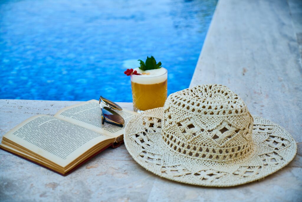 beach hat, cocktail sunglasses and book resting pool side in Los Cabos Mexico 