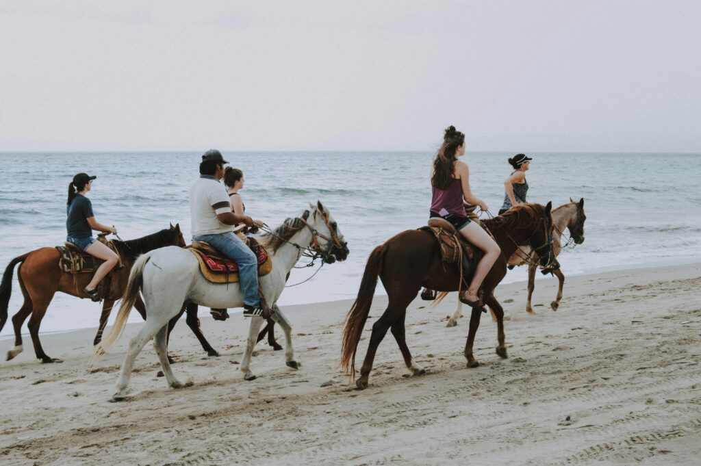 Destination Wedding Trends 2024- guests enjoying a group horseback ride along the beach 